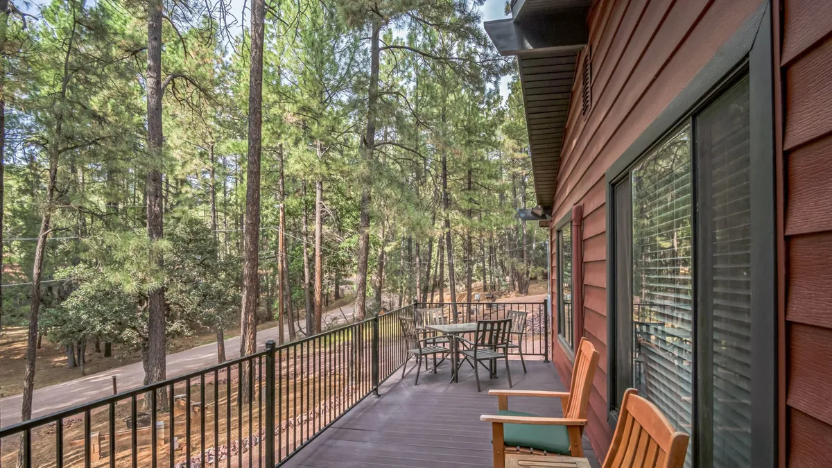 A tranquil wooden deck surrounded by lush forest, outfitted with comfortable outdoor furniture. The open sky above offers a stunning view of the stars at night or the gentle light at dusk. The scene evokes relaxation, socializing, and immersion in the natural surroundings.