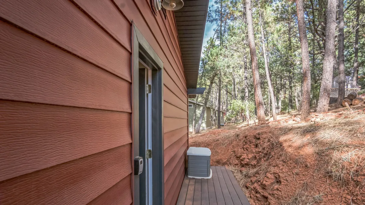 This image captures a peaceful wooden deck surrounded by mature trees. The deck is spacious and enclosed by a sturdy railing, providing a safe, open-air space for relaxing and enjoying the natural scenery. The dense greenery and tranquil vibe evoke a sense of being immersed in the mountains, perfect for both people and pets to unwind outdoors.
