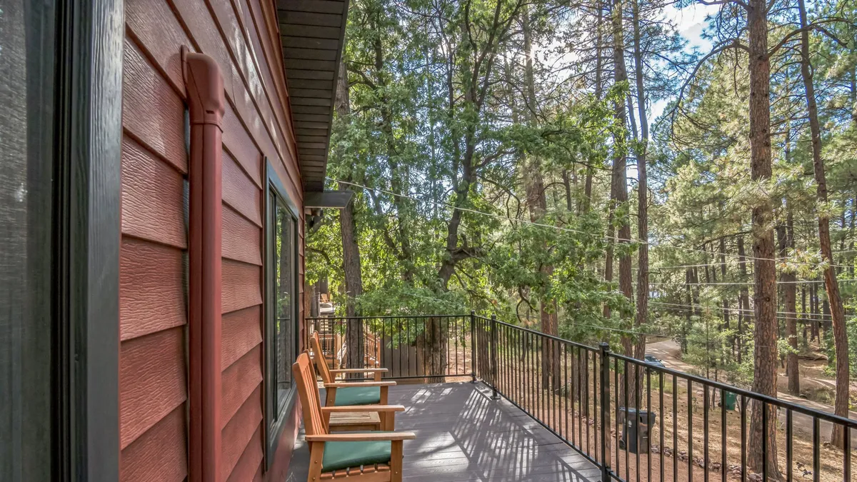 An inviting wooden balcony with classic rocking chairs overlooks a backdrop of mature trees. The vantage point allows for wildlife watching, quiet mornings with coffee, and soaking in the forest ambiance right from the comfort of home.