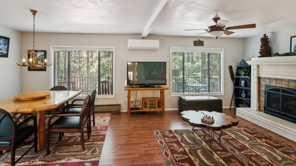 This interior image captures another angle of the open-concept living and dining area. It highlights the dining table, television, fireplace, and coffee table, arranged to support family gatherings, game nights, and cozy evenings by the fire.