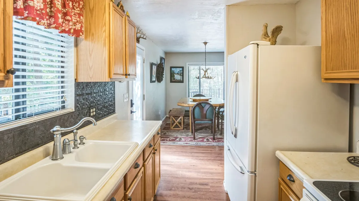 A warm and welcoming kitchen and dining setting with wooden cabinetry, a kitchen sink, an adjoining dining area, and decorative wall items. The open layout encourages both meal preparation and social interaction, conveying a homely, hospitable mood.