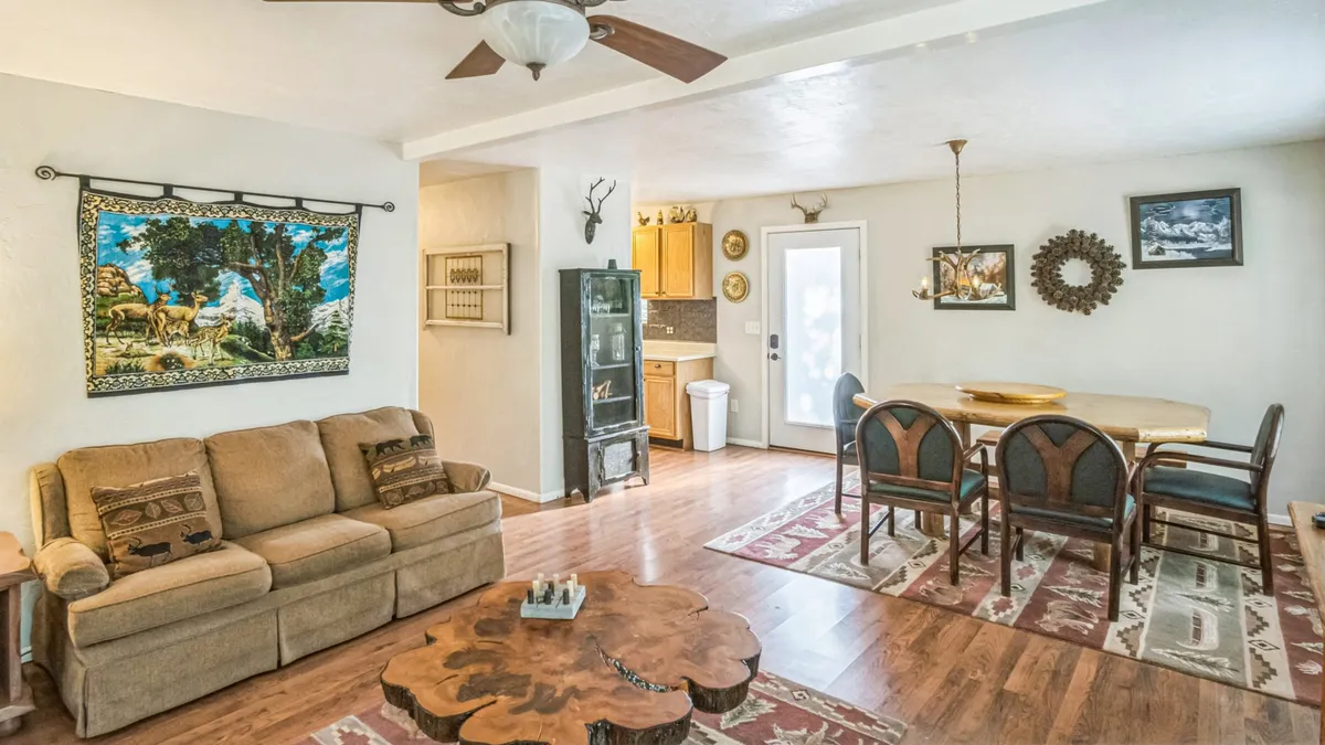 An inviting open interior with a colorful wall tapestry, wooden coffee table, and a dining area with several chairs. The arrangement is conducive to social gatherings, family meals, and group relaxation, highlighting the home's welcoming atmosphere for families exploring together.
