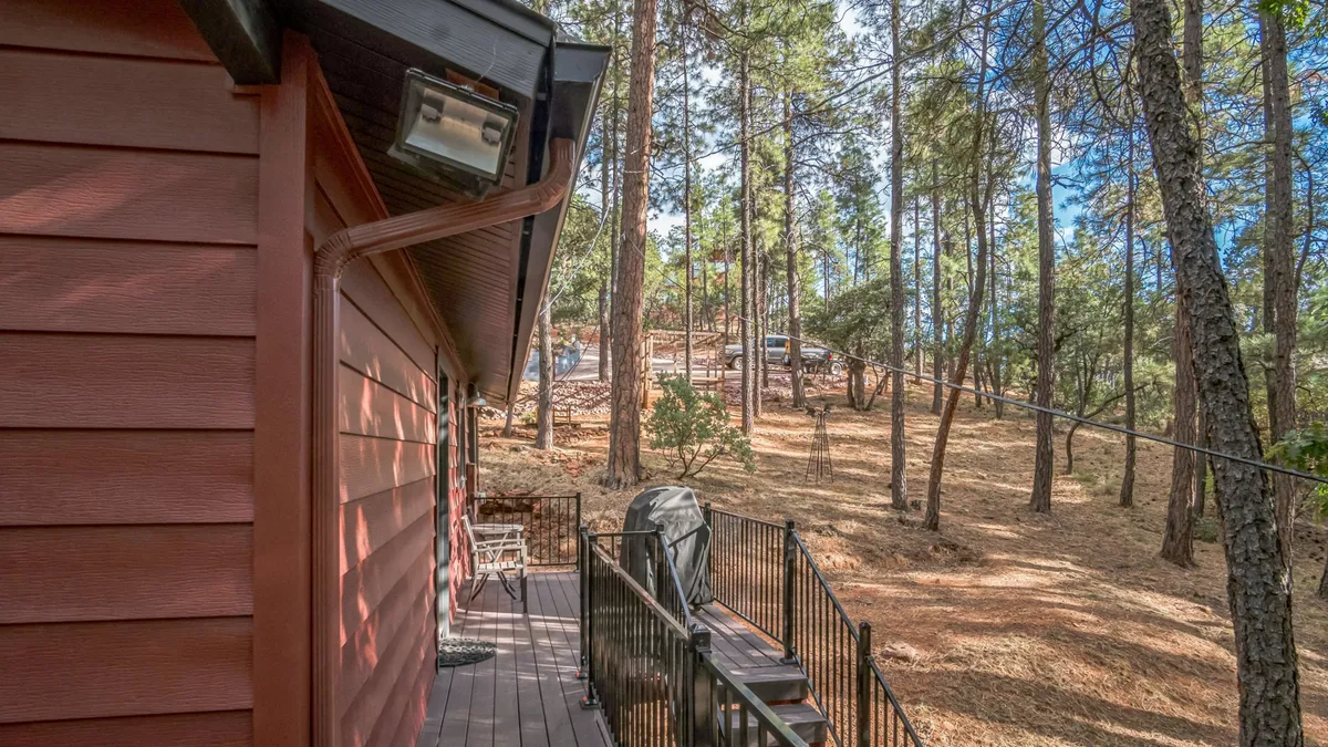 A wooden deck surrounded by lush trees, featuring an outdoor grill and comfortable seating. The deck overlooks the tranquil backyard, seamlessly blending indoor and outdoor living. The gated steps are visible, enhancing the sense of security for pets and children.