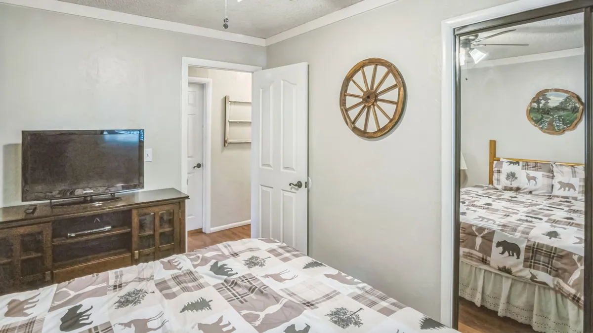 A cozy bedroom featuring a bed with a patterned quilt, a television, and a decorative wheel on the wall, with a mirror reflecting another bed. The room feels warm and inviting, suggesting comfort after a day spent exploring outdoors.