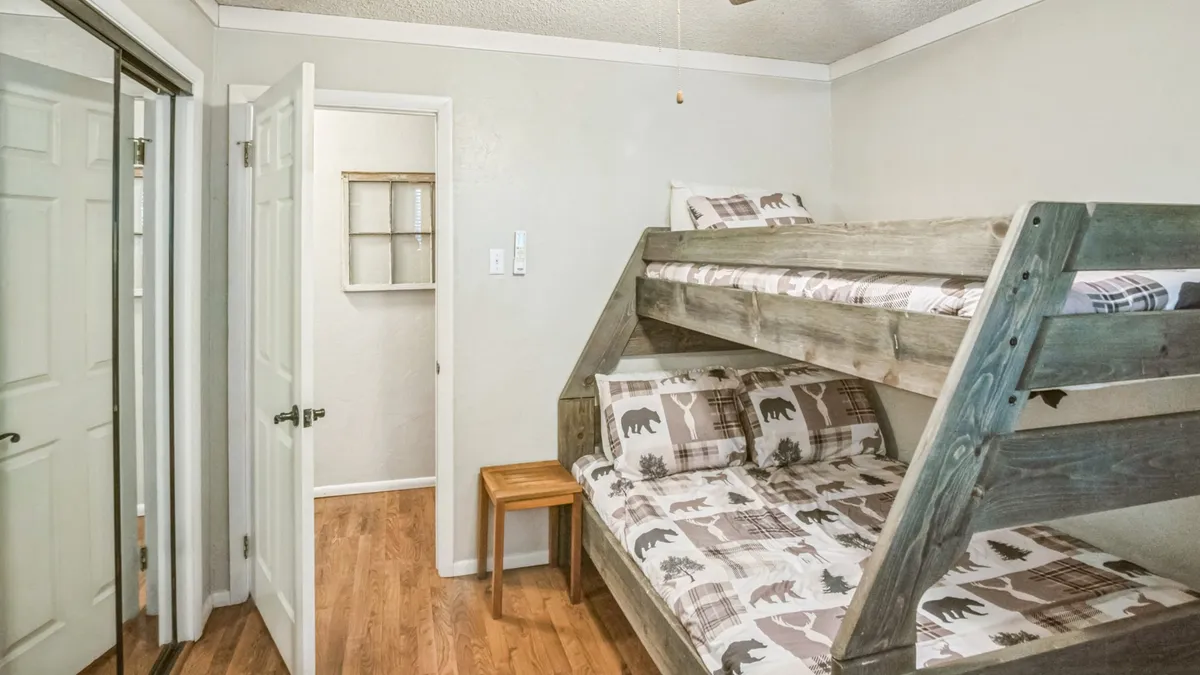 This interior scene highlights a room with a twin-over-double bunk bed, a wooden chair, and a doorway. The playful yet comfortable setup is ideal for families or groups, and the room exudes warmth and approachability.